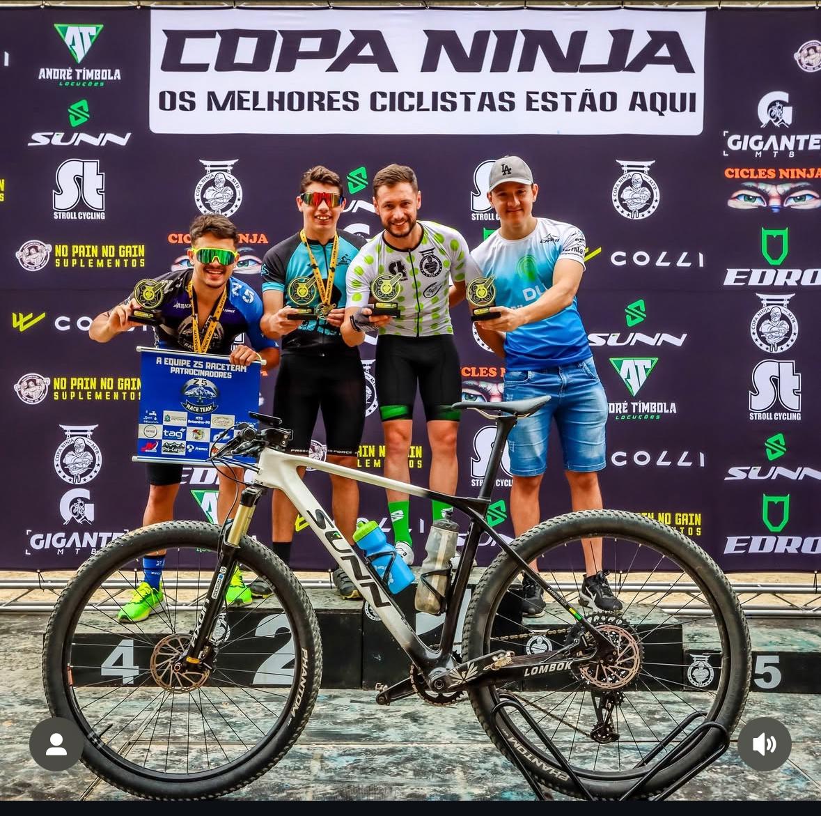 Atletas no pódio da Copa Ninja com troféus e mountain bike SUNN em primeiro plano