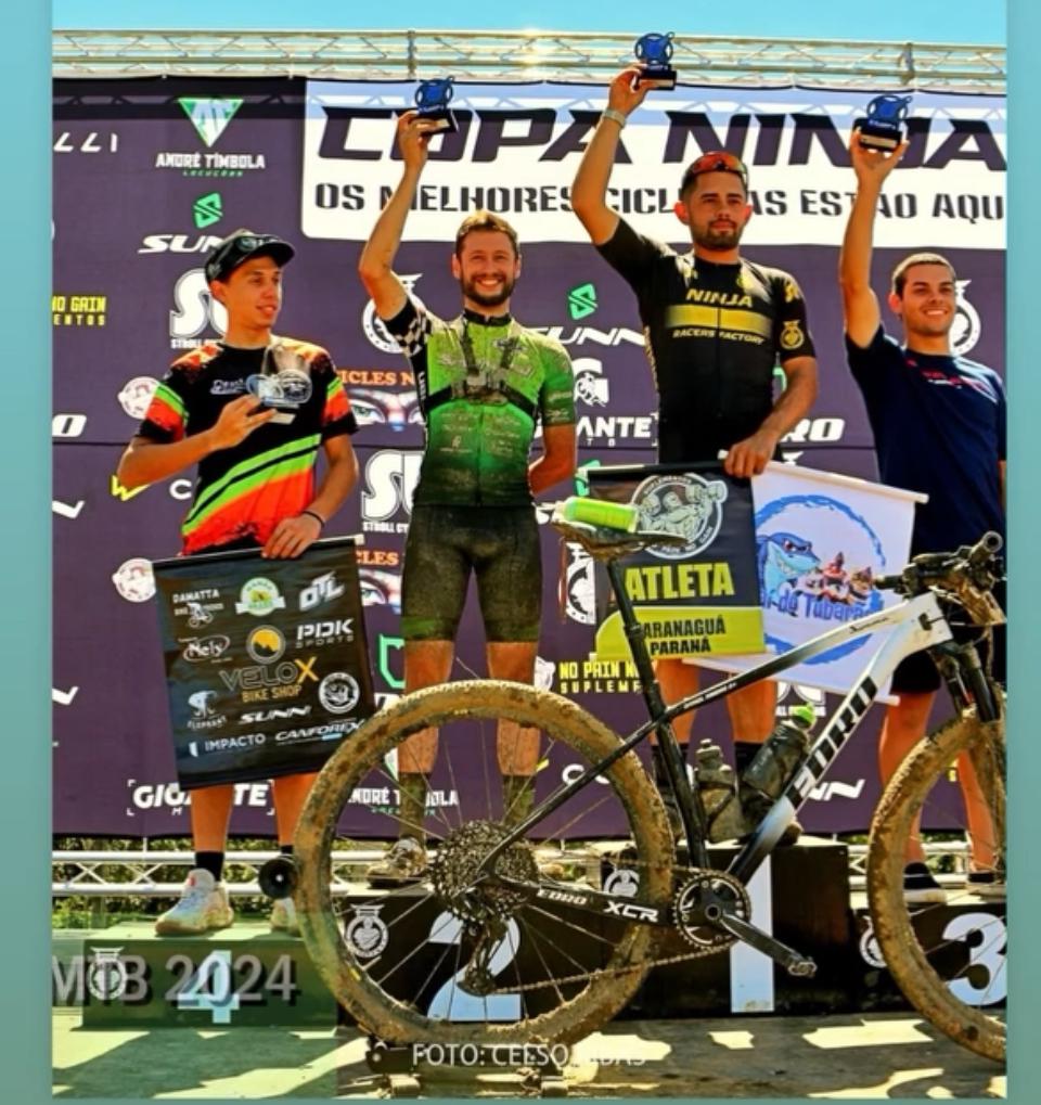 Pódio da Copa Ninja com atletas celebrando e mountain bike com lama em primeiro plano