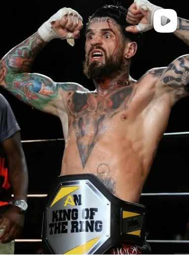 Lutador de Muay Thai tatuado comemorando vitória no ringue com o cinturão King of the Ring